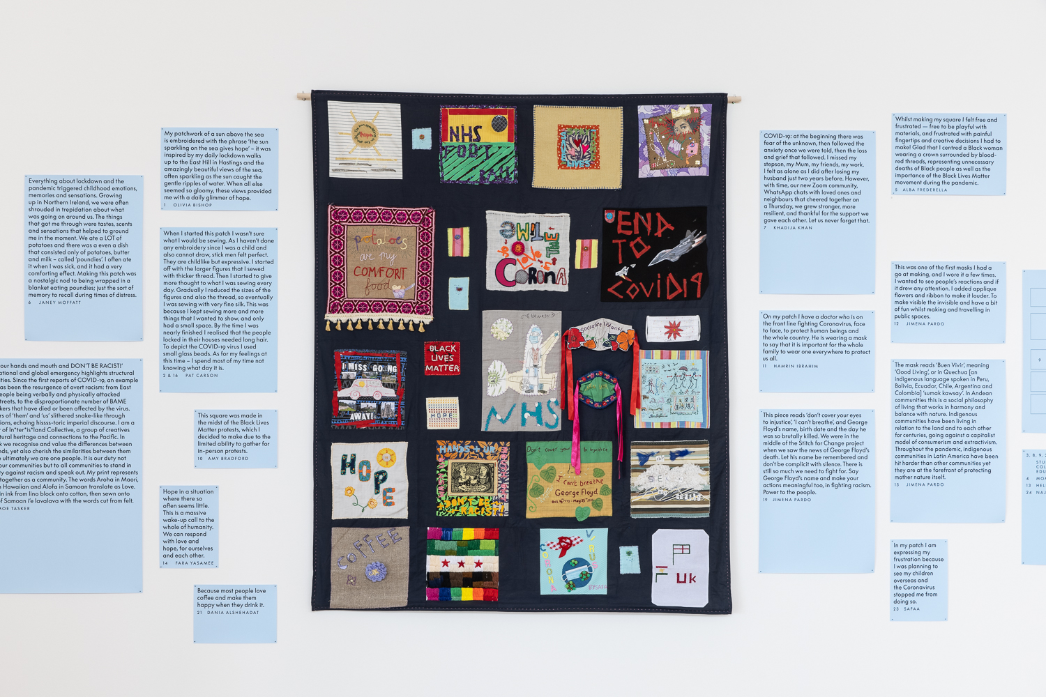 Image of a black quilt with a series of hand sewn patch work squares hanging on a wall, and text on each side of display 
