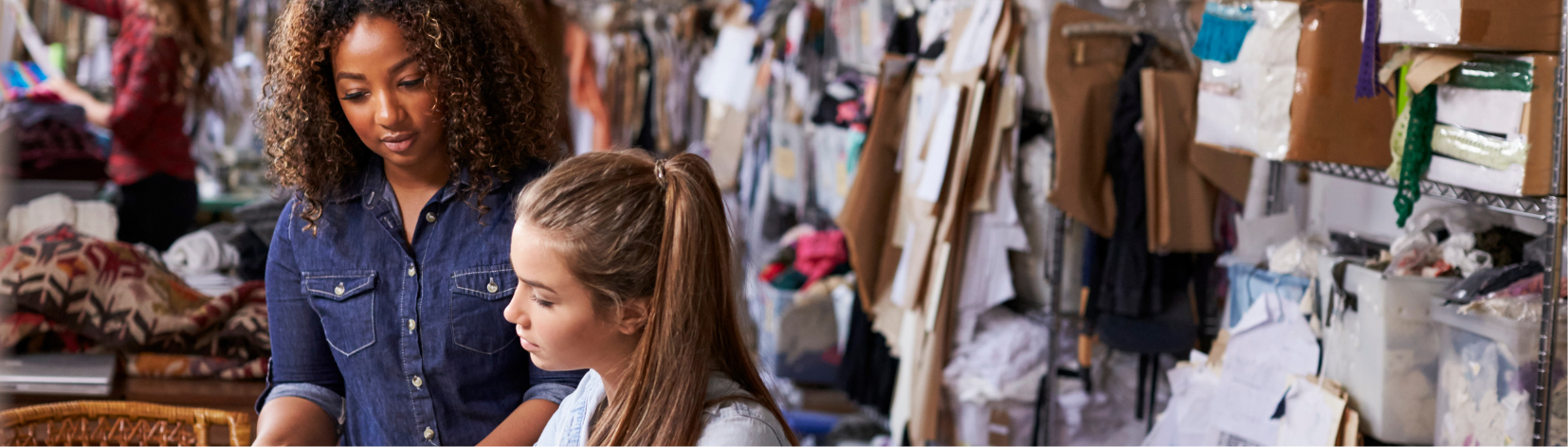 Two people standing in a room filled with textiles. 