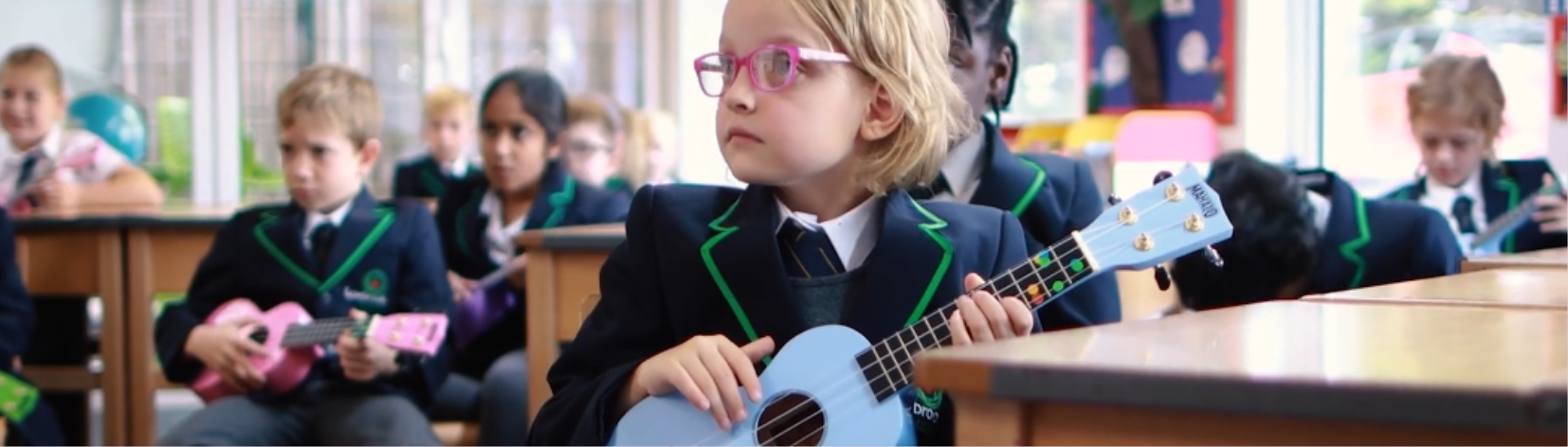 Children in school uniform holding miniature guitars.