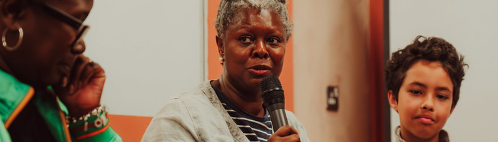 Three people sat in a row, the person in the centre is speaking into a microphone.