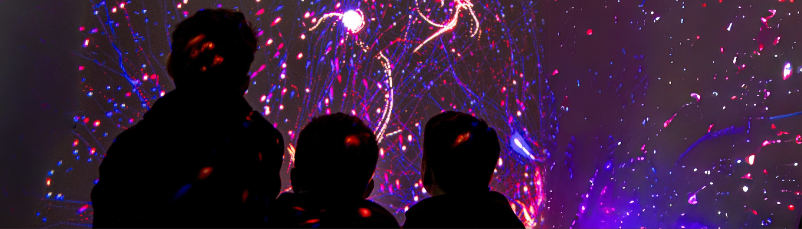 Silhouettes of three children looking at a projection of pink and purple lights.