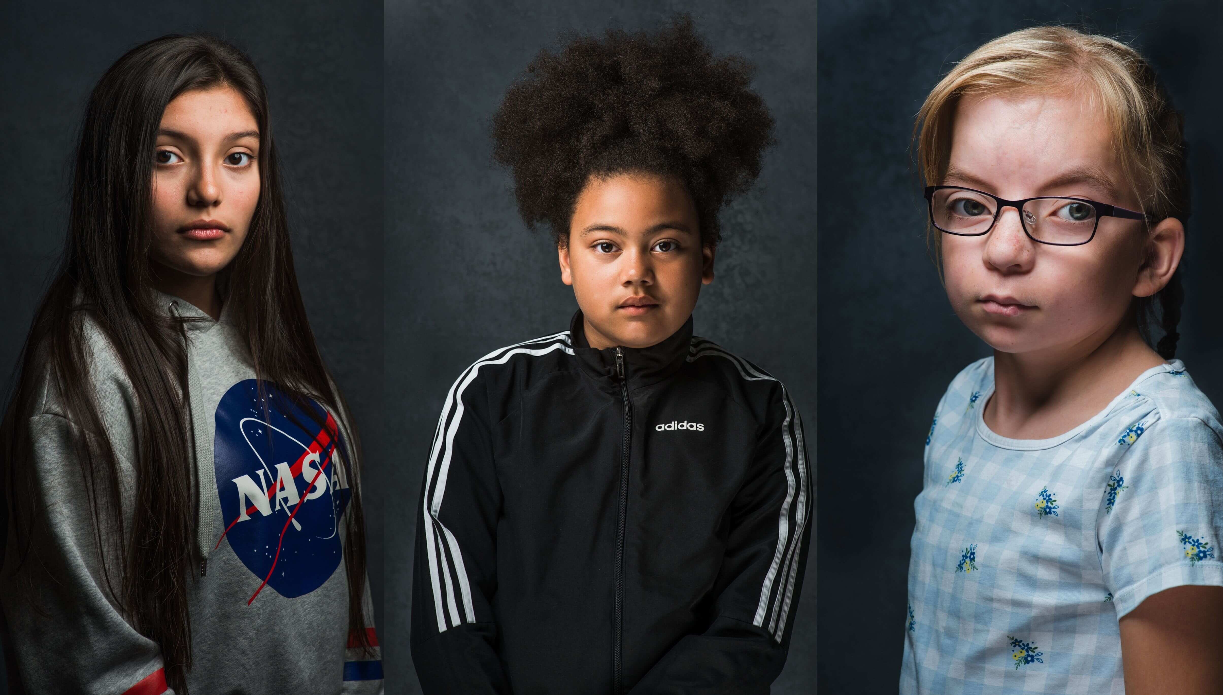 Three portrait pictures of three girls from Bradford, each standing against a black background – as part of the Impression Gallery’s current exhibition, Being Inbetween by Carolyn Mendelsohn. 