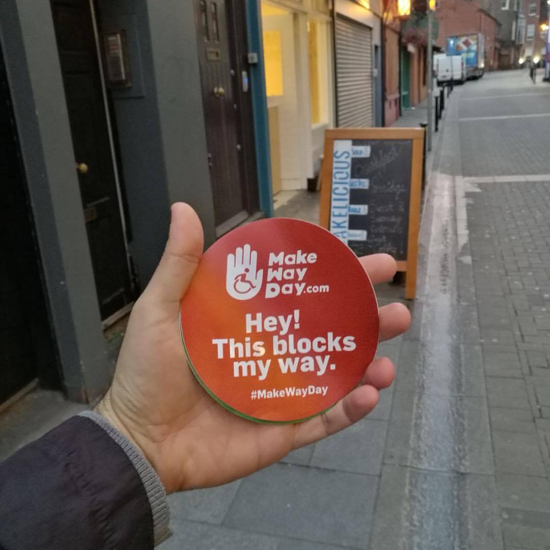 A hand holding a circular Make Way Day sticker reading 