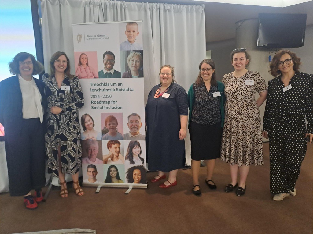 Six women standing together smiling beside a banner reading 